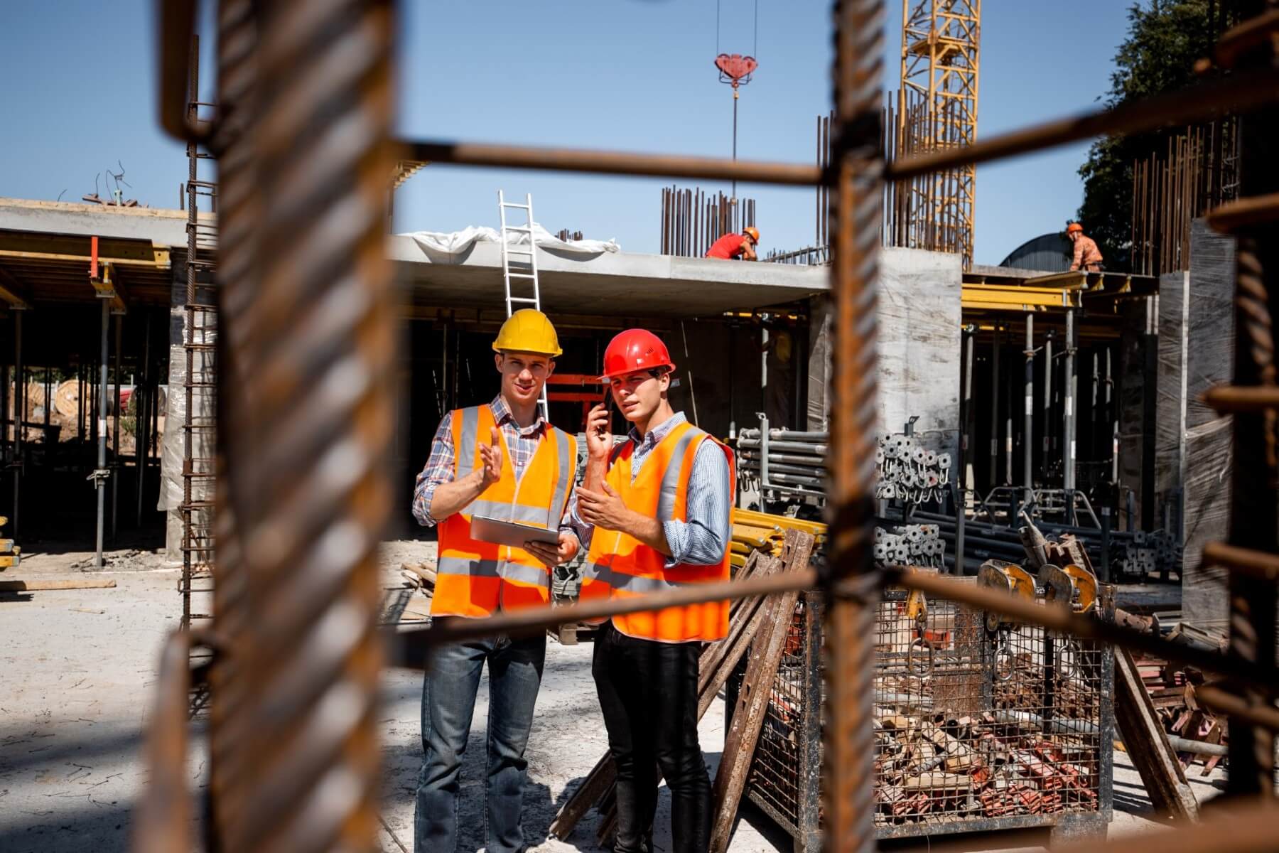 Reinforcing steel cage in the foreground with workers reviewing the concrete structure behind