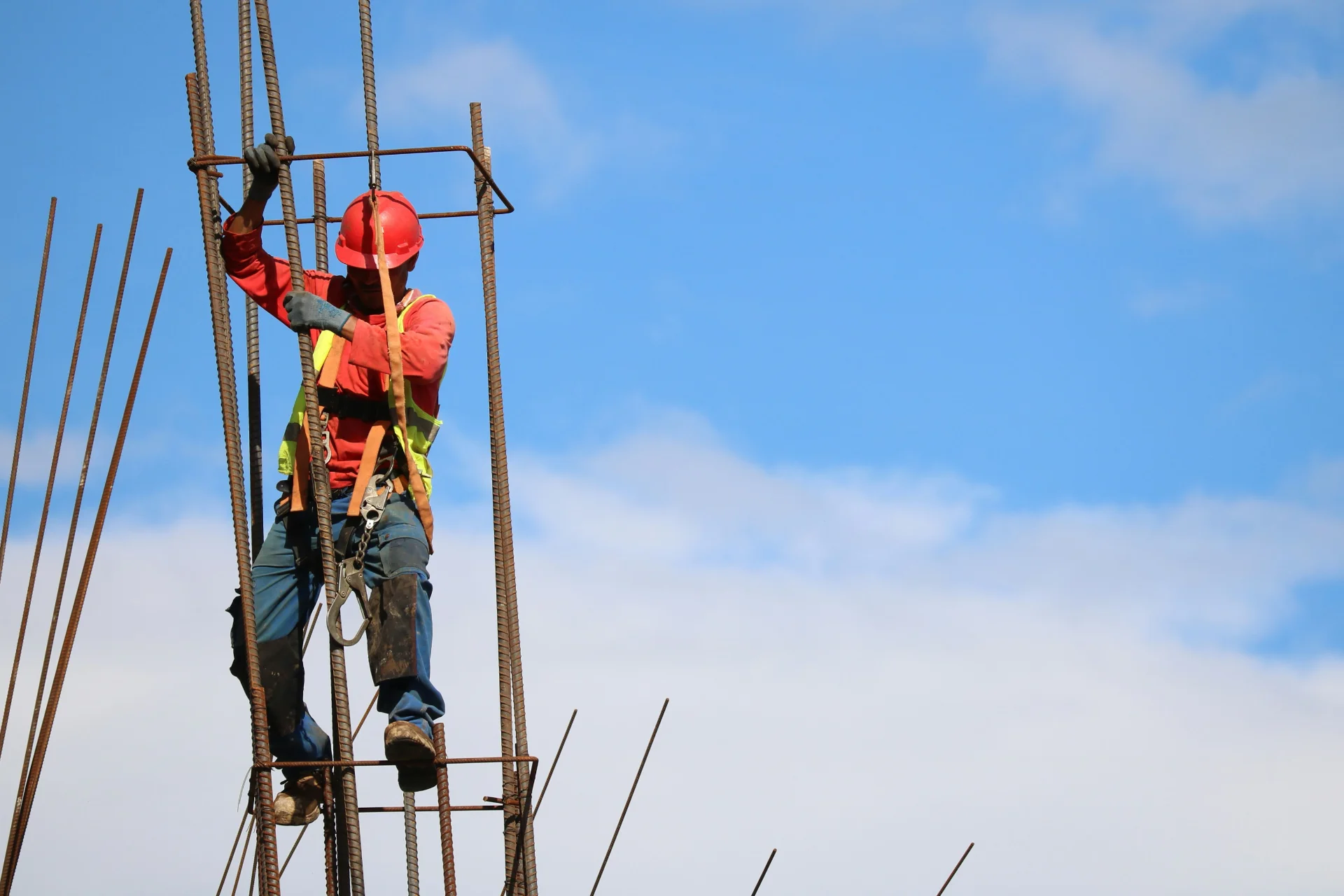 Ironworkers tying reinforcing steel at the top of a column cage against an open sky