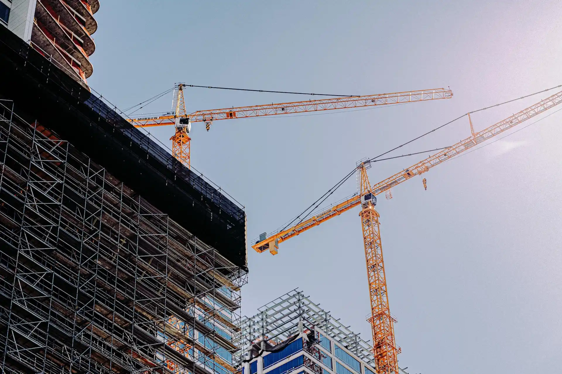 Tower cranes beside a steel floor structure viewed from below on a construction site