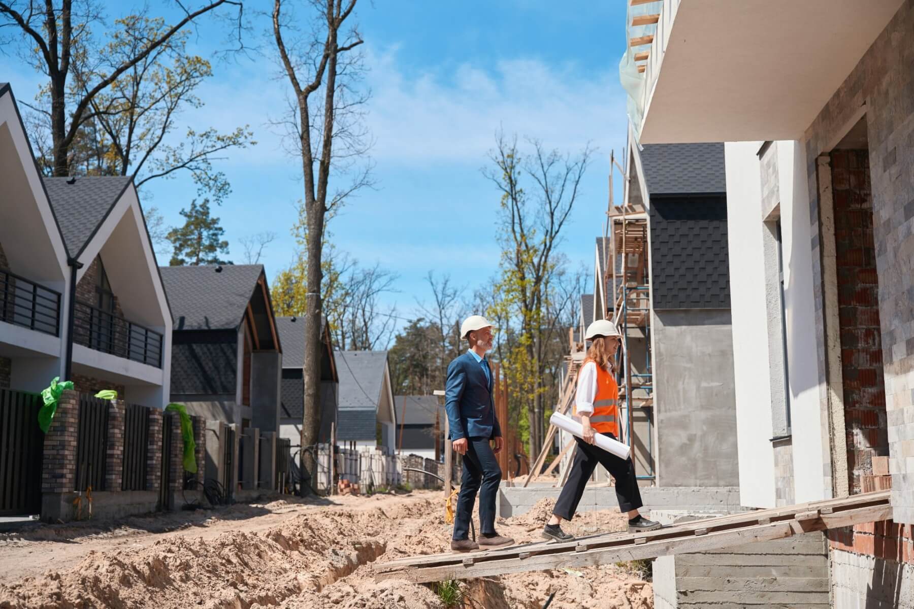Wood-framed houses under construction in a row with workers walking the site
