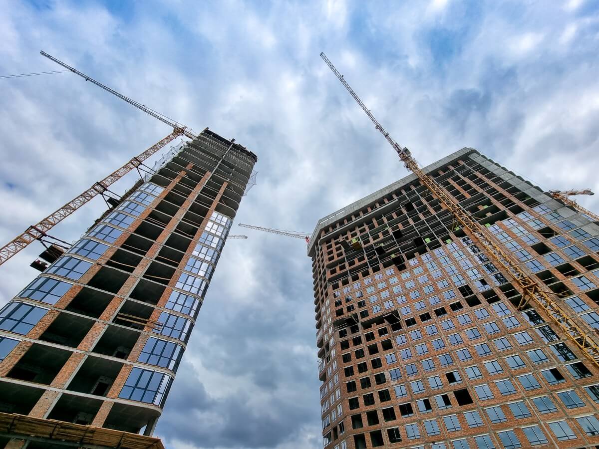 Two concrete high-rise structures under construction seen from ground level with formwork and tower cranes