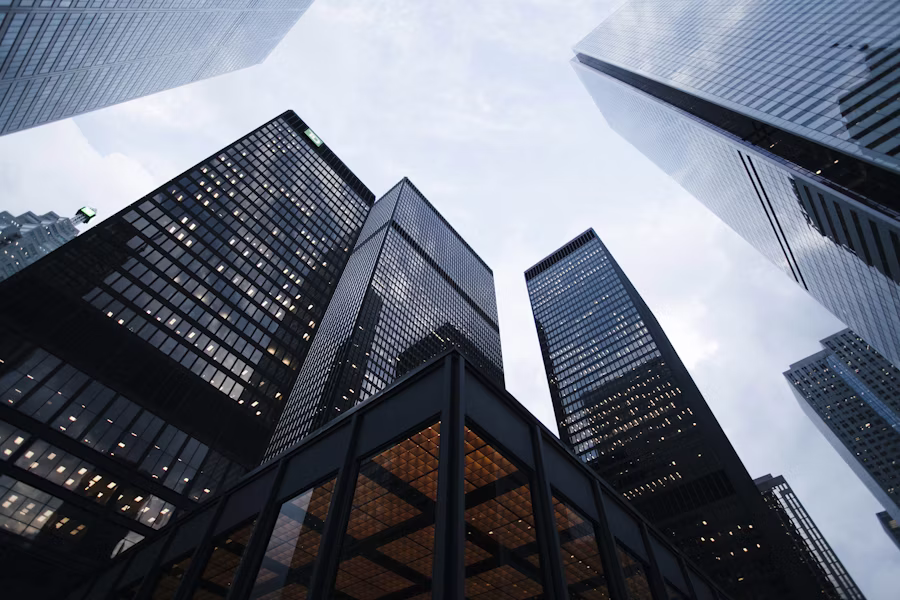 Low-angle view of tall glass office skyscrapers towering over the viewer against a cloudy sky, urban canyon scene.