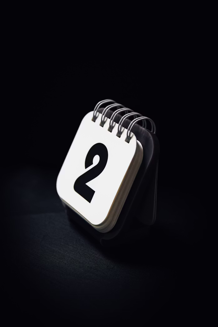 Mini desktop calendar displaying the number 2 on a white card, set against a dark background.